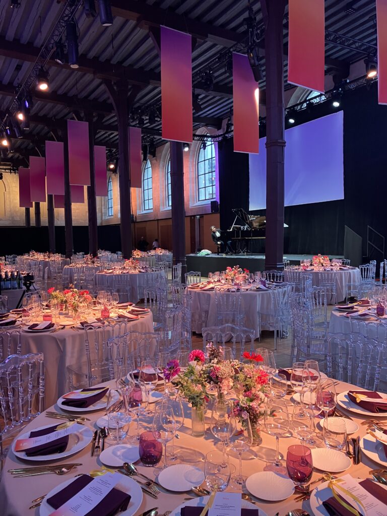 Repas assis pour un dîner avec scène et concert piano. Eclairage scénique à l'image de l'événement.